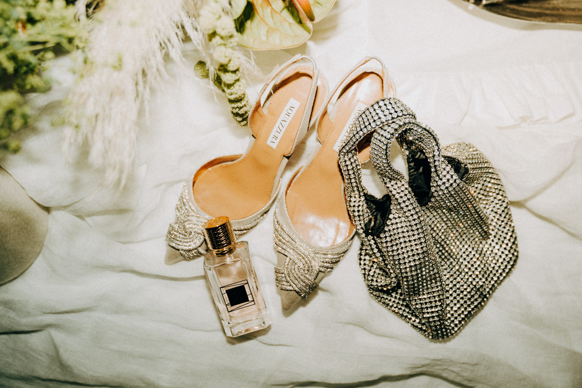 Schicke Glitzerschuhe, ein teures Parfum und eine glitzernde Brauthandtasche auf einem Tisch arrangiert