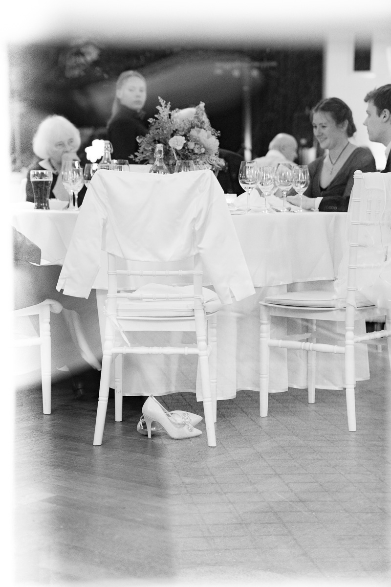 Durch ein Fenster fotografiert, ausgezogene Hochzeitsschuhe und eine Hochzeitsgesellschaft beim Tanzen